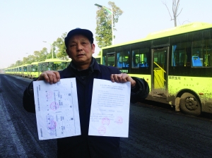 劉明手持多個部門的審批文件，身后就是閑置在路邊的電動公交車